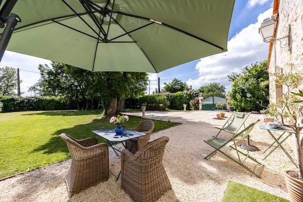 Eine Terrassesituation mit Korbmöbeln, einem Tisch mit Blumenvase und einem großen Sonnenschirm.
