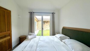 Ein Hotelzimmer mit einem Bett, einem Holzschrank und Blick auf ein Steingebäude durch eine Glastür.