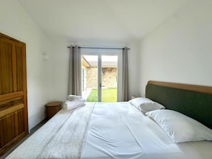 A hotel room with a bed, a wooden wardrobe, and a view of a stone building through a glass door. - VILLA CAPU - 5 BDRMS WITH POOL AND GARDEN (Lecci)