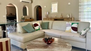 Ein modernes Wohnzimmer mit einem beigefarbenen Ecksofa, einem Glastisch und einem Couchtisch aus Marmor.