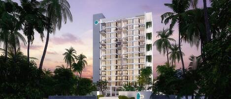 A modern multi-story hotel with a grid-like facade, surrounded by palm trees and greenery.