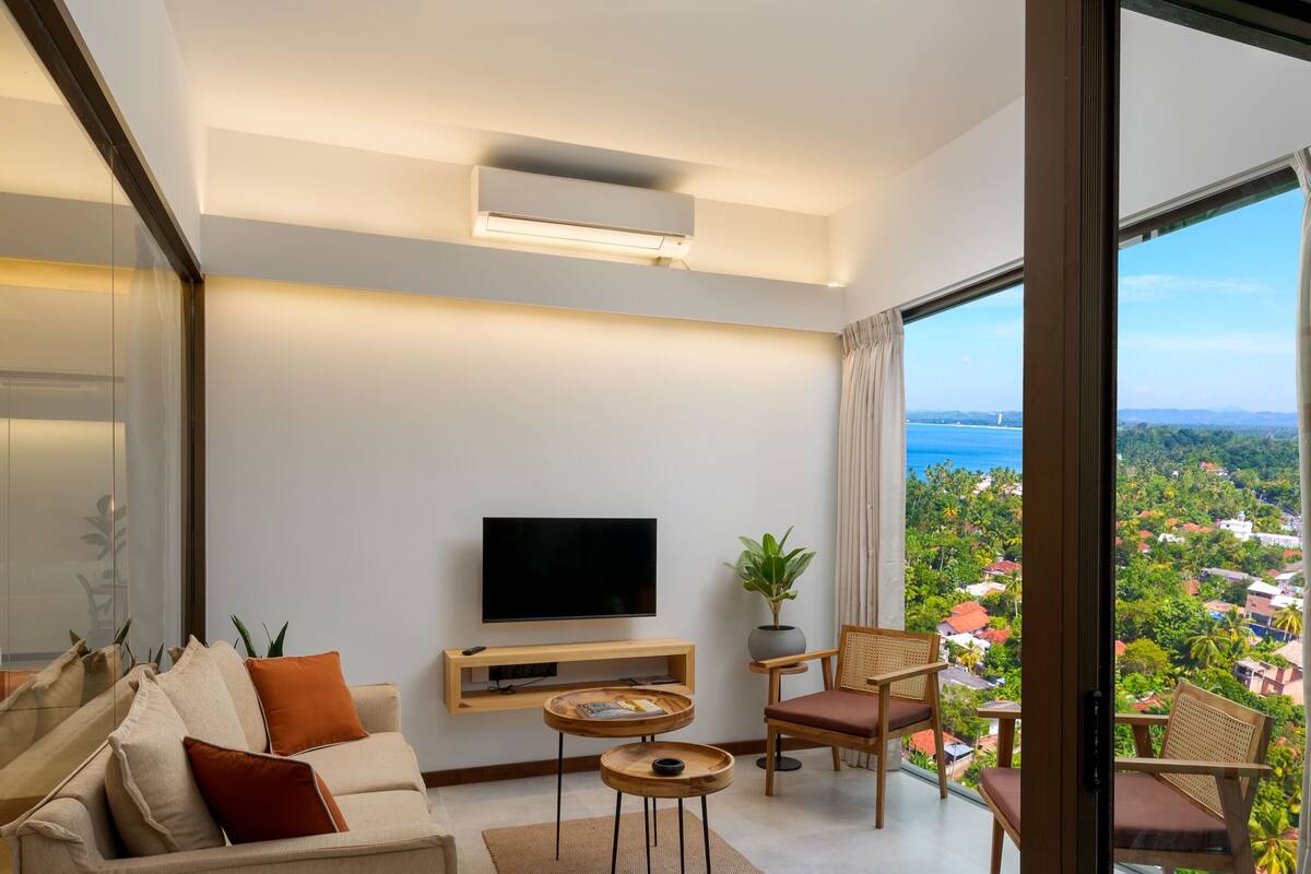 A modern living room with a sofa, TV, and a balcony with a view.