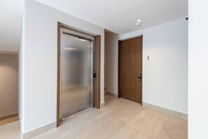 A hallway with a modern elevator and a wooden door, leading to a staircase. - Mojarra 27: Bright, Centric Suite w/Balcony -NEW (Cancún)