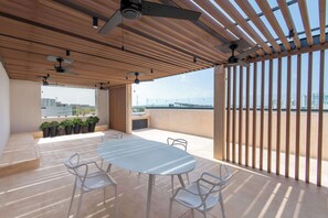 An outdoor terrace with a table and chairs, a ceiling fan, and a view of the cityscape. - Mojarra 27: Bright Studio in Downtown Cancún (Cancún)