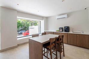 A modern kitchen with a dining area, featuring a large window, a built-in air conditioner, and a coffee machine. - Mojarra 27: Bright Studio in Downtown Cancún (Cancún)