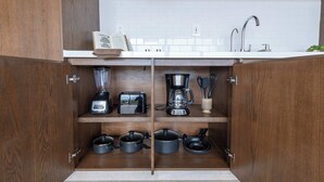 A kitchen with wooden cabinets, a white countertop, a coffee maker, a blender, and pots. - Mojarra 27: Apt. with Balcony & King Bed (Cancún)