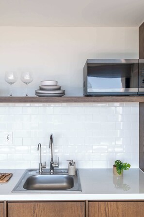 A modern kitchen with a stainless steel sink, white tiled backsplash, and a microwave on the countertop. - Mojarra 27: Cozy Apartment with Balcony (Cancún)