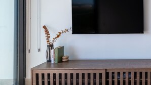Ein modernes Wohnzimmer mit einem großen Flachbildfernseher an einer weißen Wand, einer Holzbänklage mit Stauraum und einem großen Fenster, das für natürliches Licht sorgt.