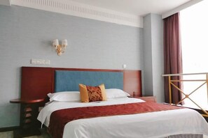 Habitación de hotel con una cama grande, una mesita de noche, una lámpara de pared y un ventanal con cortinas.