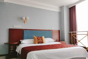 Habitación de hotel con una cama grande, una mesita de noche, una lámpara de pared y un ventanal con cortinas.