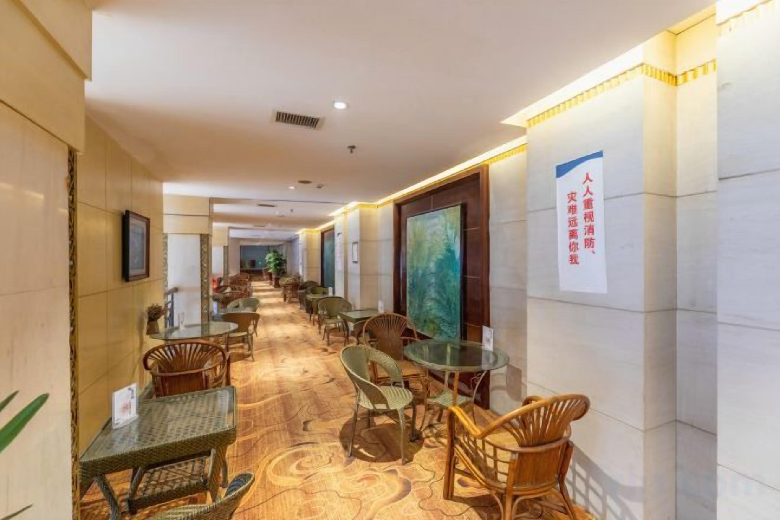 Un pasillo de hotel con sillones de mimbre, mesitas de vidrio y piso alfombrado.