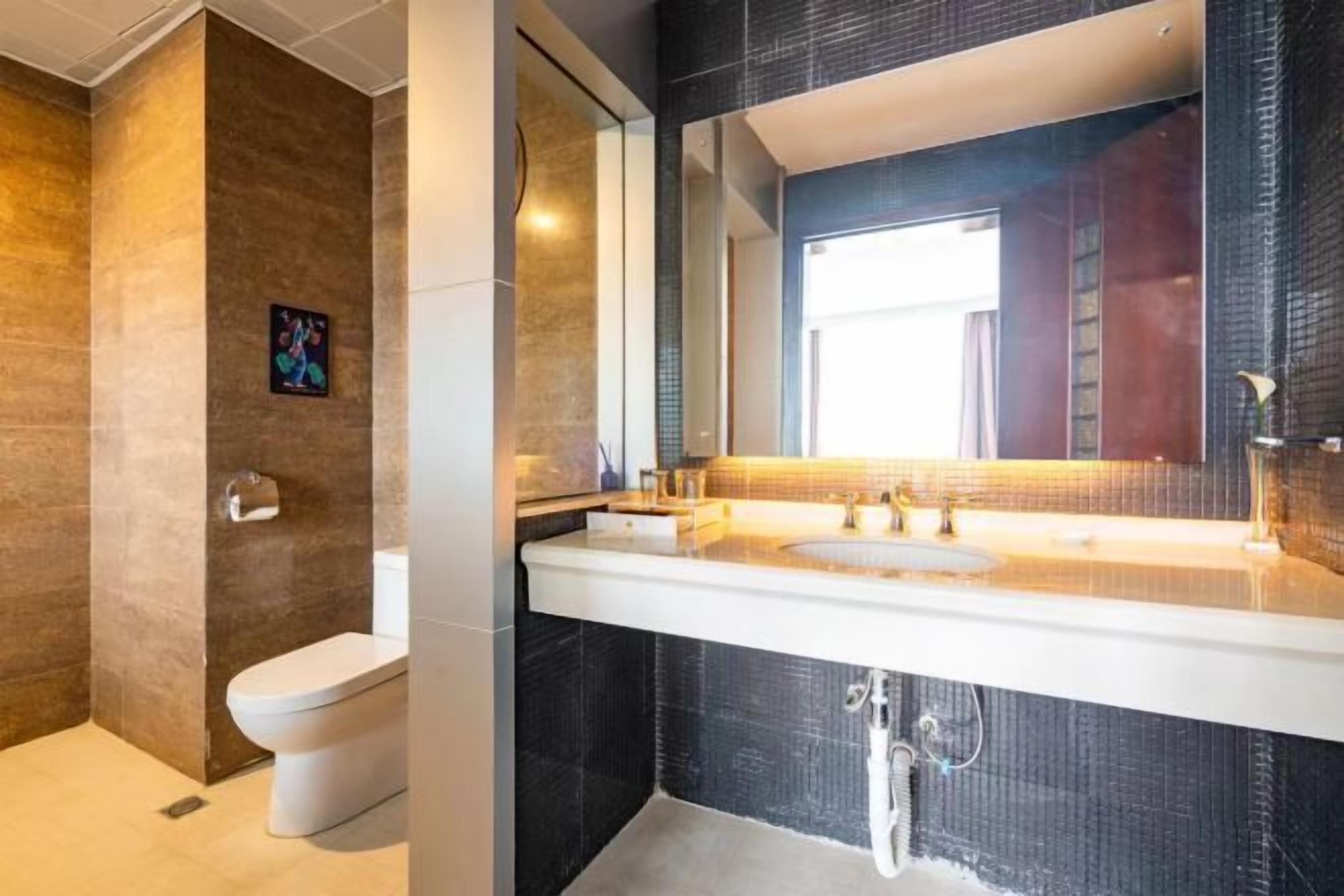 A modern bathroom with a large mirror, white sink, and dark tiled walls.