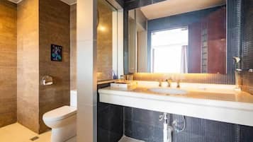 A modern bathroom with a large mirror, white sink, and dark tiled walls.