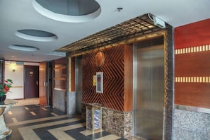 A hotel lobby with a reception desk, a wall-mounted elevator, and a patterned wall design. - Anshun Kaixuan Hotel (Nanma Plaza) (Anshun)
