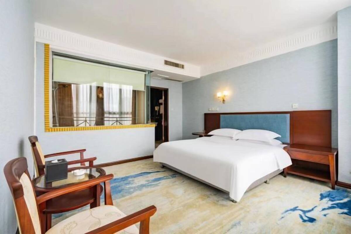 A hotel room with a bed, a desk, a chair, and a large mirror.