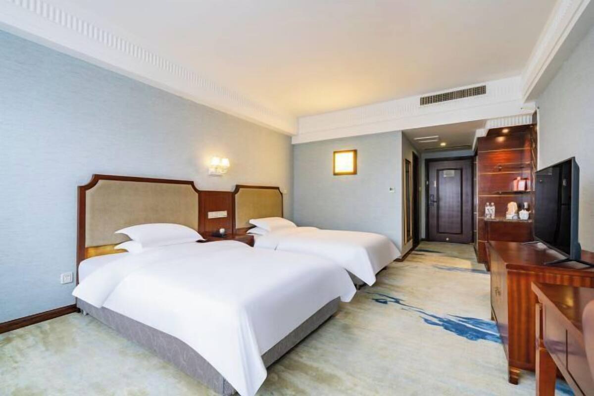 A hotel room with two beds, a television, and a desk.