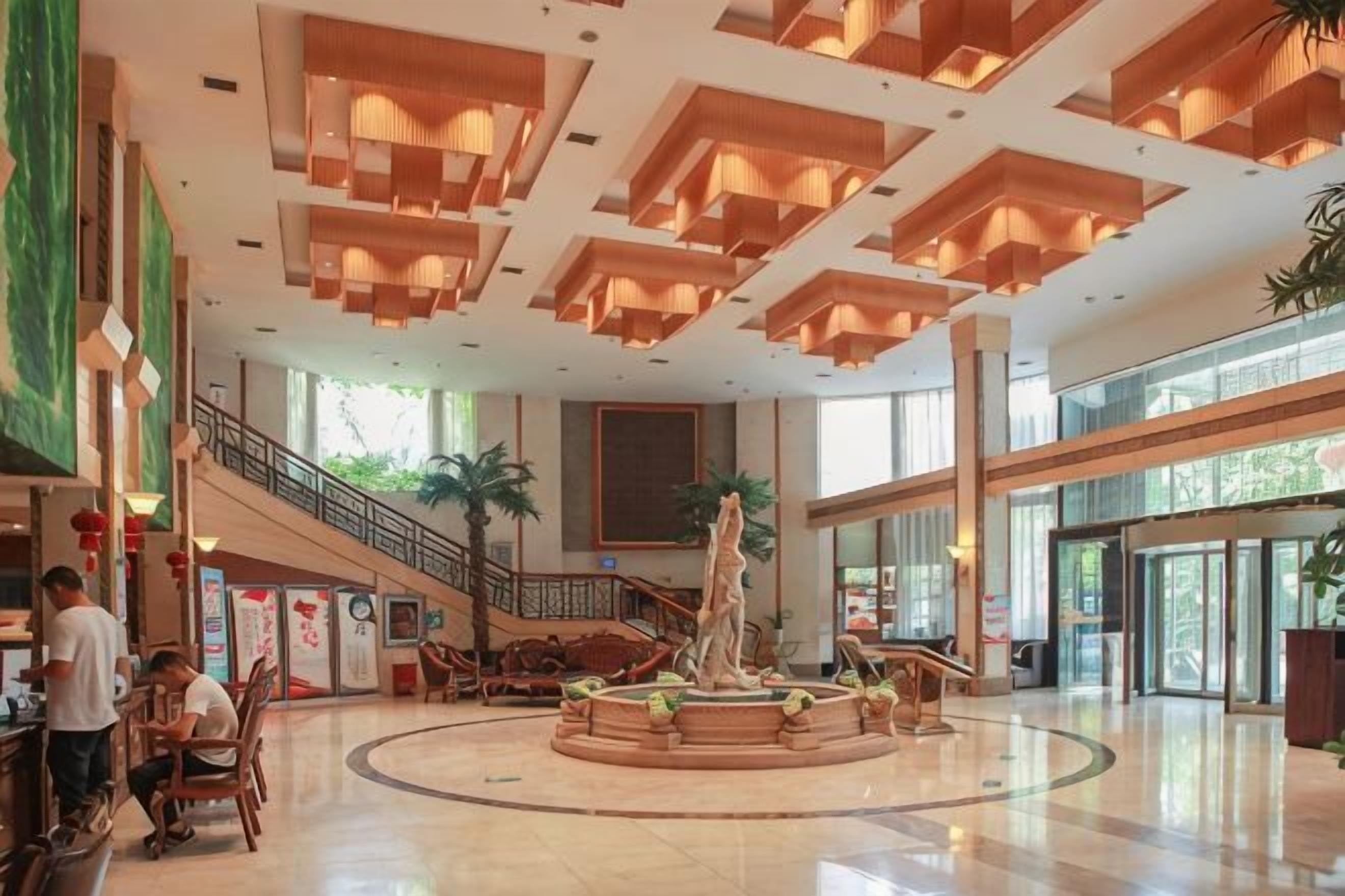 Um lobby amplo com uma fonte central, escadaria e áreas de estar.