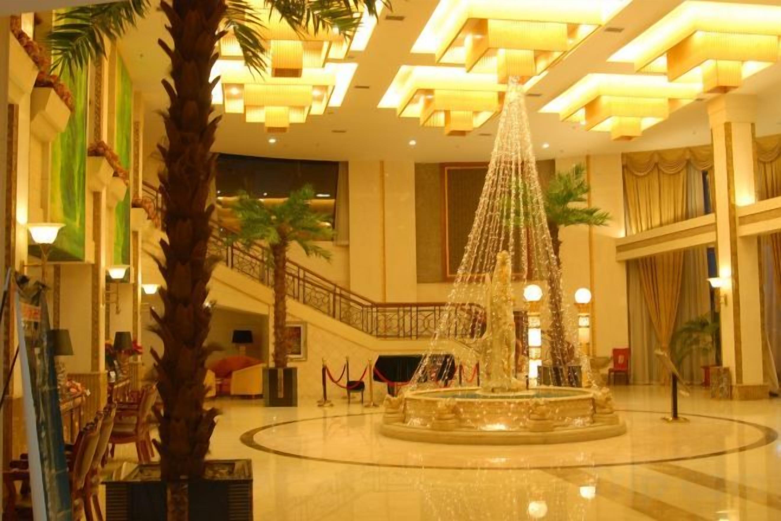 A lobby with a central fountain, a palm tree, and a staircase.