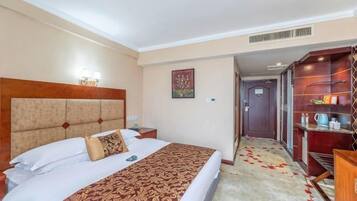A hotel room with a bed, bedside table, lamp, and a small shelf with items.