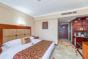 Een hotelkamer met een bed, nachtkastje, lamp en een klein plankje met spullen.