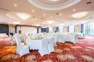 Un salón de banquetes con mesas redondas, sillas blancas y una alfombra roja.