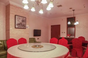 Un comedor con una mesa redonda, sillas rojas, un sofá verde y un televisor en la pared.