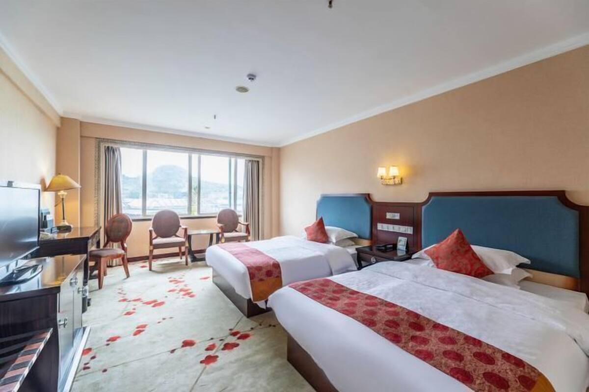 A hotel room with two beds, a desk, a TV, and a window with a view.