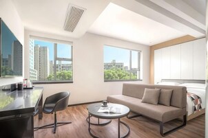 Una habitación de hotel moderna con sofá, una mesita redonda, escritorio y cama.