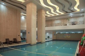 Une grande piscine intérieure dotée d’un plafond aux motifs ondulés, de plusieurs niveaux et offrant une vue sur l’étage supérieur.