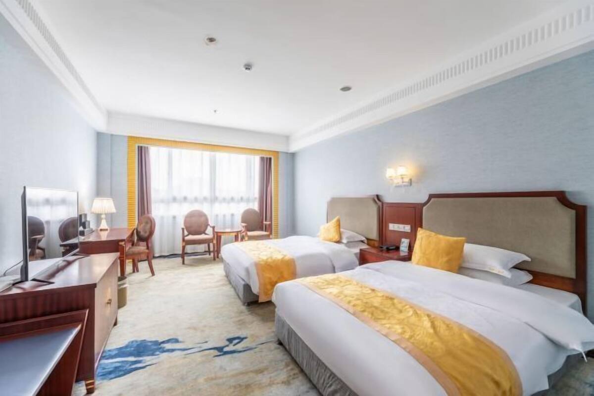 A hotel room with two beds, a desk, a chair, a TV, and a window with curtains.