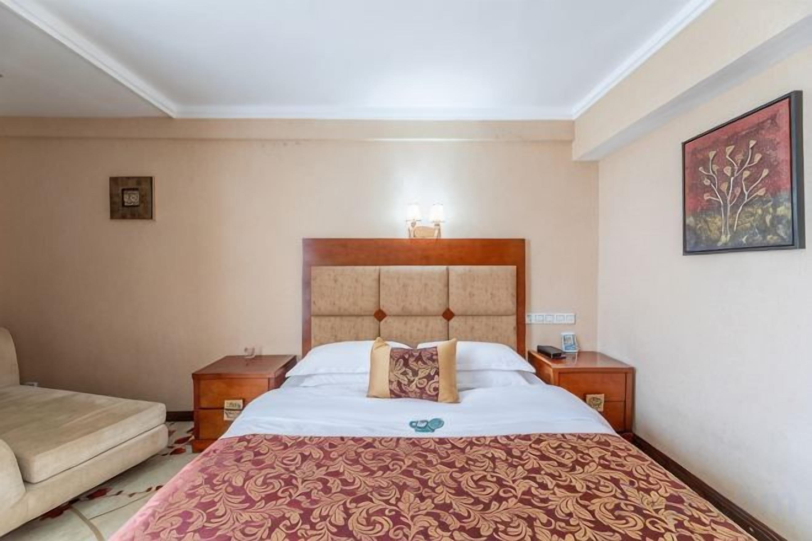 A hotel room with a bed, a nightstand, a chair, and a painting on the wall.