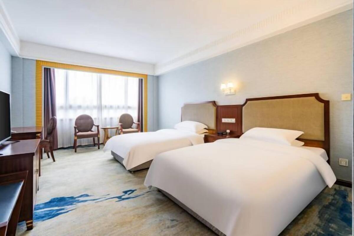 A hotel room with two beds, a desk, a chair, and a TV.