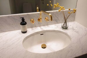 A bathroom with a white marble sink, gold faucets, and a bottle of shampoo. - Nyhavn63 Premium Apartment 1 Daniel&Jacob's (København)