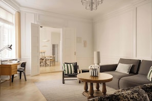 A modern living room with a sofa, a round coffee table, a desk with a chair, and a dining area in the background. - Nyhavn63 Suites - Canalside - 4 Bedrooms (København)
