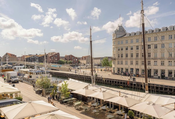 A riverside view with a tram, buildings, and outdoor seating areas. - Nyhavn63 Suites - Canalside - 4 Bedrooms (København)