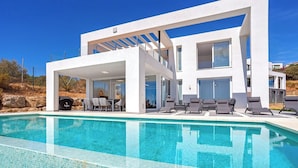 Een modern huis met een zwembad, buitenmeubilair en een helderblauwe lucht.