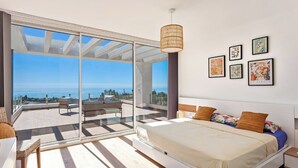 Een moderne slaapkamer met een groot bed, een balkon met uitzicht en kunst aan de muur.