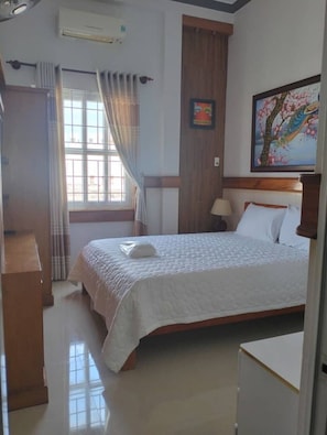 Hotelkamer met een bed, een bureau, een raam met gordijnen, een schilderij aan de muur en een airconditioning.