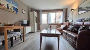 Un salón con una mesa de centro de madera, un sofá de cuero marrón, un televisor sobre un mueble de madera y una ventana con cortinas.