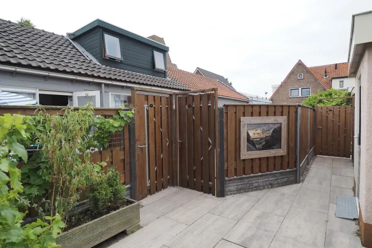 Un quartier résidentiel avec une clôture en bois, un jardin planté d’arbustes et un toit recouvert de tuiles.