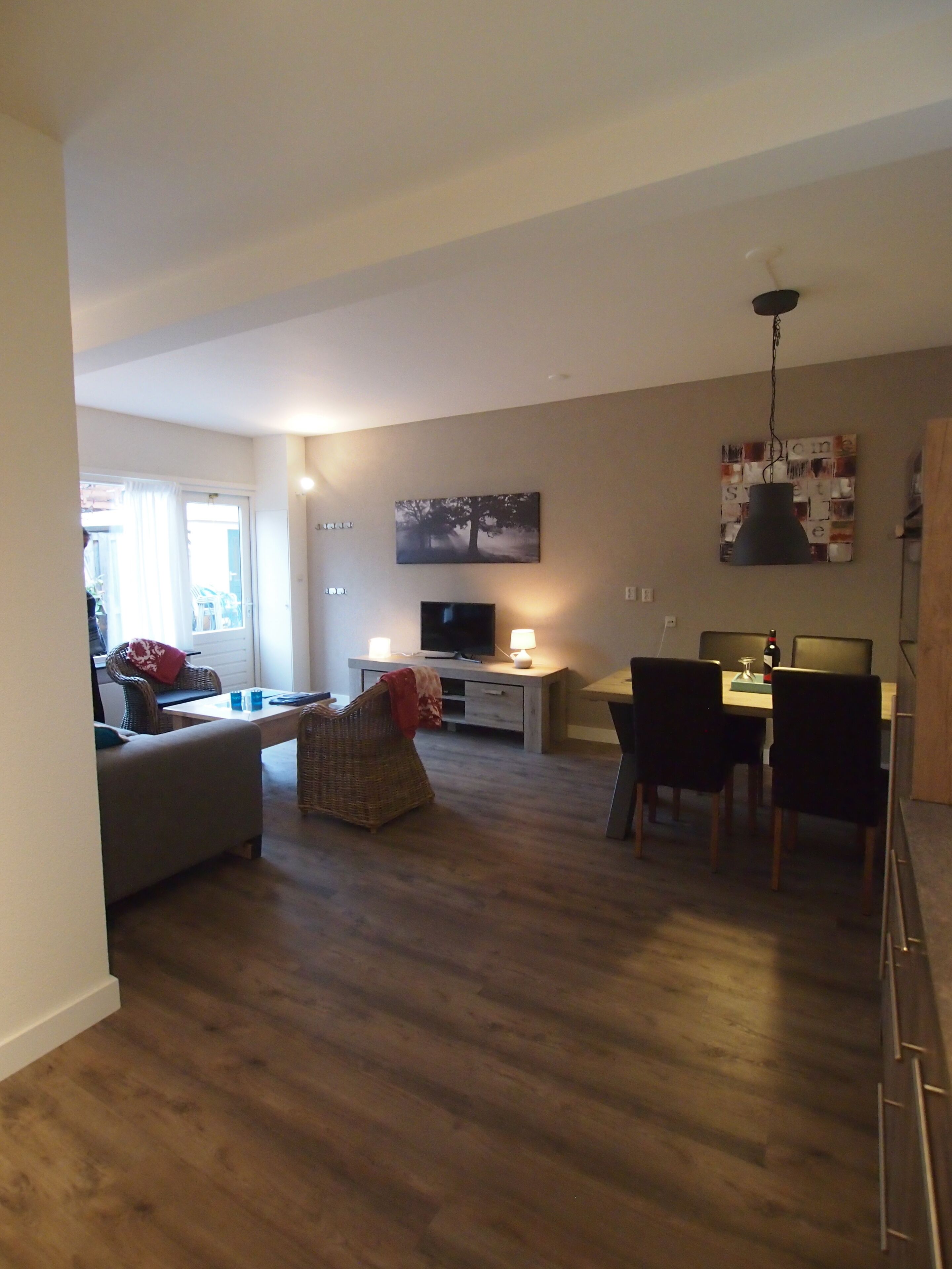 A modern living room with a flat-screen TV, a dining area with a table and chairs, and a large window with curtains.