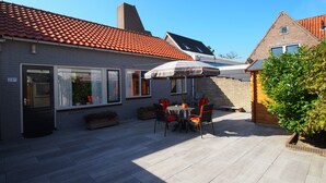 Ein Innenhof mit Terrassentisch und -stühlen, ein Backsteinhaus mit Ziegeldach und eine kleine Holzkonstruktion.