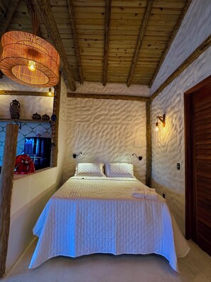 Ein Bett mit weißer Bettdecke, darüber eine gewebte Lampe und eine rustikale Holzbalkendecke.