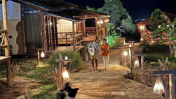 A rustic outdoor pathway leading to a wooden building with a tiled roof, surrounded by greenery and illuminated by hanging lights. - Vila Calm Bungalows - Serra da Ibiapaba - Views of the mountains and the city. (Várzea do Giló)