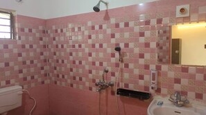 A bathroom with a checkered tile wall, a shower, a sink, and a mirror. - The Kolam (Bolpur)