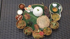 A traditional South Indian meal with rice, curries, and flatbreads on a banana leaf. - The Kolam (Bolpur)