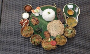 A traditional South Indian meal with rice, curries, and flatbreads on a banana leaf. - The Kolam (Bolpur)