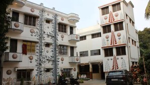 A multi-story hotel with balconies, a parking area, and decorative patterns on the facade. - The Kolam (Bolpur)