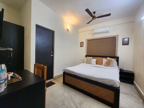 A bedroom with a bed, a desk, a chair, a ceiling fan, a door, and a wall-mounted air conditioner. - The Kolam (Bolpur)