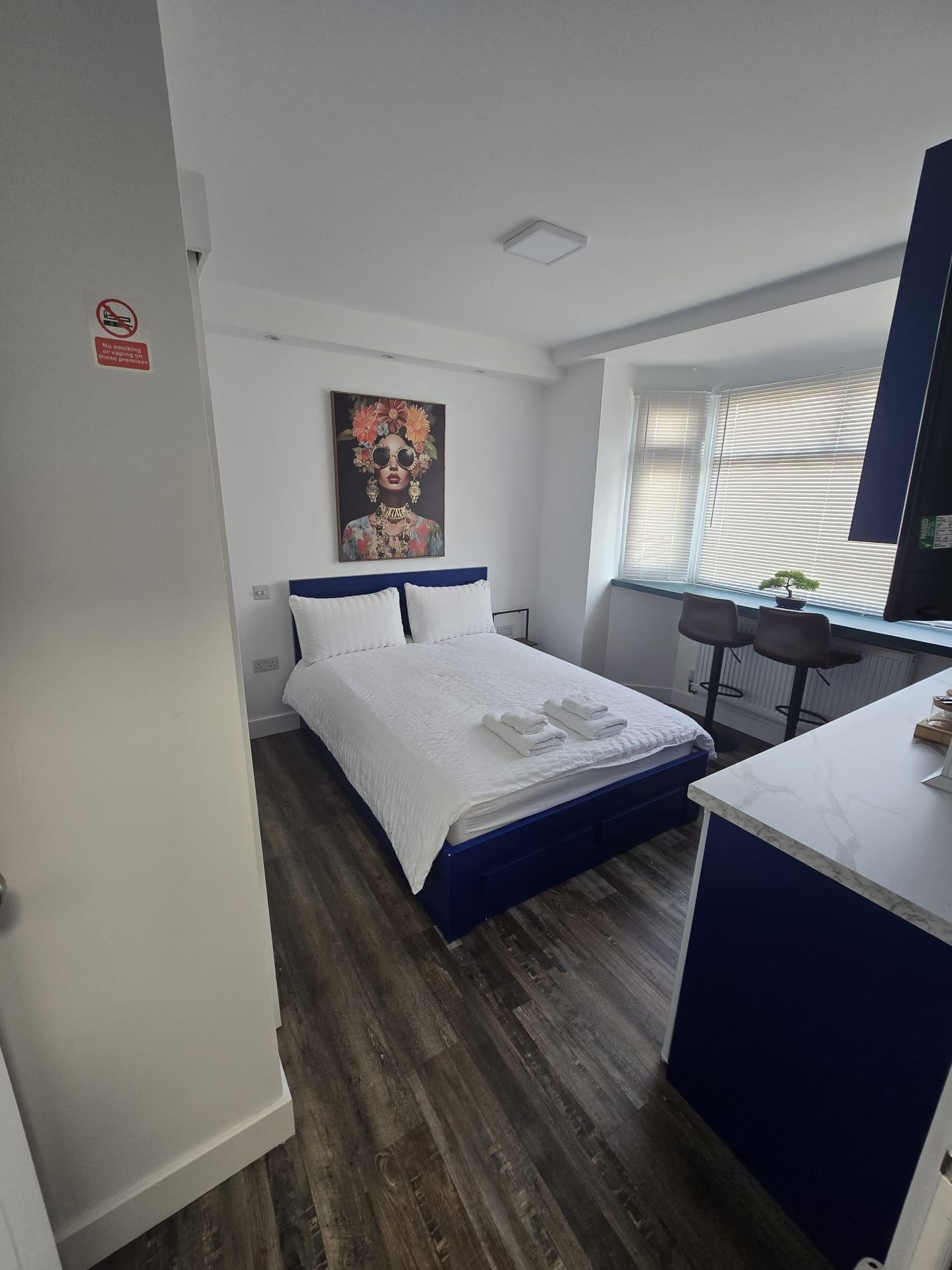 A bedroom with a bed, a desk, and a window with blinds.